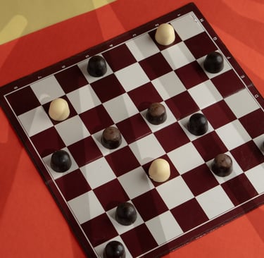 A game of checkers played with dark and white chocowell chocolates on a classic red and white board.