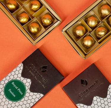 Gourmet gold foil-wrapped chocolate truffles in gift boxes on an orange background.