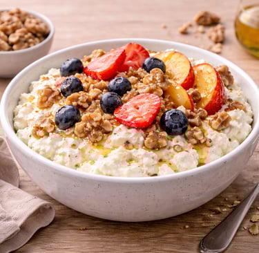 Bol de requesón con nueces, fruta fresca y un toque de miel, desayuno saludable alto en proteína.
