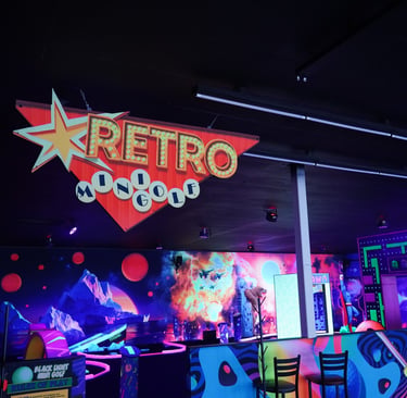 A glowing neon retro mini golf sign hanging over a blacklight indoor putt-putt course.
