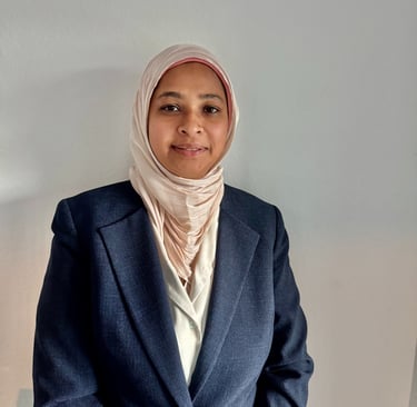Professional portrait of a smiling woman wearing a pink hijab and dark blue blazer.