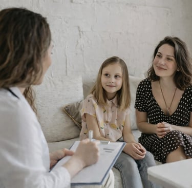 Profissional de saúde com prancheta realiza uma consulta de acolhimento com uma mãe e sua filha no consultório