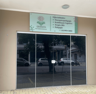 Fachada da Clínica Granata com porta de vidro espelhada e placa de identificação verde. Na placa, lêem-se as especialidades.