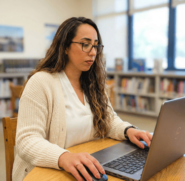 Julie Granata de óculos e cardigã claro trabalhando em um notebook em ambiente de consultório