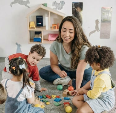 Profissional de saúde, Julie Granata, sentada no chão de uma sala, interagindo com crianças pequenas usando blocos de montar