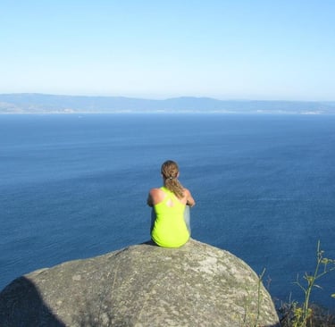 a woman sitting on a rock in front of a body of water