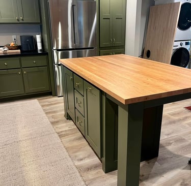 Modern green kitchen cabinets with a butcher block island and stainless steel refrigerator.