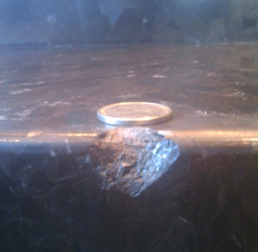 A small chip on the edge of a dark marble countertop next to a silver coin for scale.