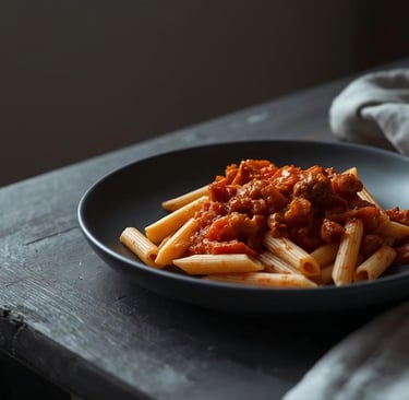 Tomato and sausage penne served in a matte ceramic bowl on a dark rustic wooden table