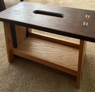 Handcrafted walnut and oak wood step stool with carry handle and decorative joinery on a carpeted floor.
