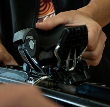 A technician's hands adjusting black Xpress ski bindings on a pair of downhill skis for safety.
