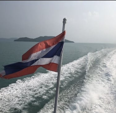 Die thailändische Flagge weht auf einem Boot auf dem Meer, mit tropischen Inseln und weißer Gischt