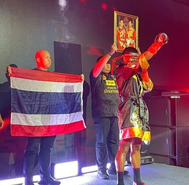 Ein Muay-Thai-Kämpfer in traditioneller Robe hält auf einer beleuchteten Bühne ein Porträt