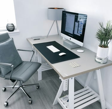 Modern home office setup with a gray ergonomic chair, white trestle desk, and an iMac computer.