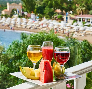 Refreshing summer drinks and sliced fruit platter on a balcony overlooking a tropical beach resort.