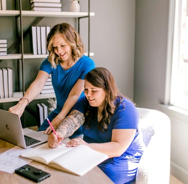 Two business women collaborating in a modern office with a laptop and notebook.
