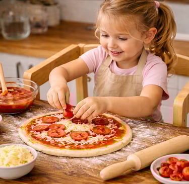 bambina su. una torre di apprendimento mentre prepara una pizza in cucina.