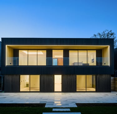 Modern black timber clad house with illuminated glass balconies and large windows at dusk.