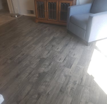 Modern dark gray wood-look luxury vinyl plank flooring installed in a living room with an armchair and media console.