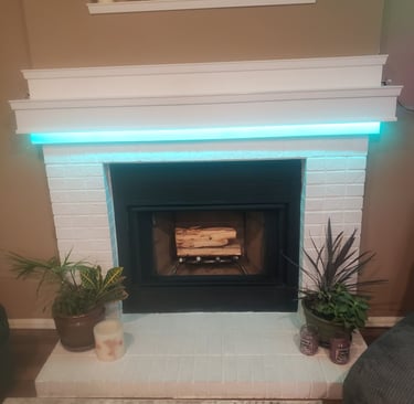 Modern white painted brick fireplace featuring teal LED mantel lighting, decorative candles, and indoor plants.