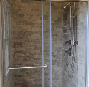 Modern walk-in shower featuring natural stone subway tile walls and a sliding glass door.