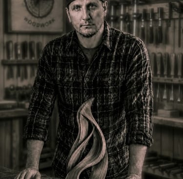 Owner of Tree Ring Woodwork, Isaac Griffin, in front of a wooden sculpture in a workshop.