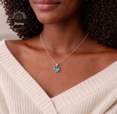 A woman wearing a silver chain necklace with a heart-shaped aquamarine crystal pendant.