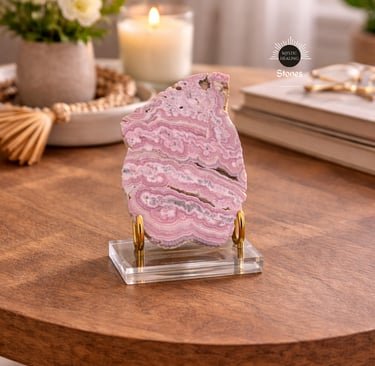 Polished pink rhodochrosite crystal slice on a gold and acrylic display stand on a wooden table.