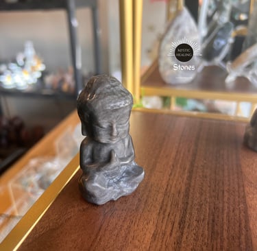 Smoky Obsidian Buddha statue in a meditating pose on a wooden shelf for spiritual decor.