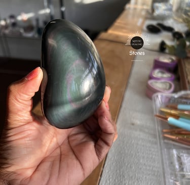Polished velvet obsidian palm stone with iridescent pink and green sheen held in hand.