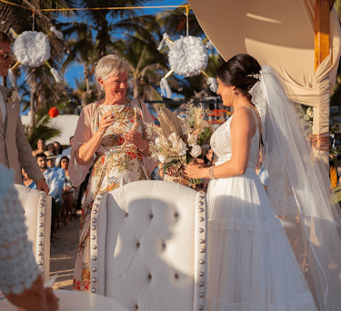 Bride and groom at an outdoor beach wedding ceremony under a canopy with palm trees.