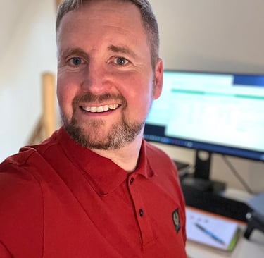 Mike Brown in a red polo shirt working at a home office desk with a computer monitor.