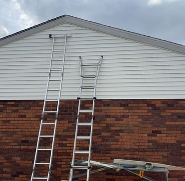 Two aluminum extension ladders leaning against a house with white siding and brick for home repair work.