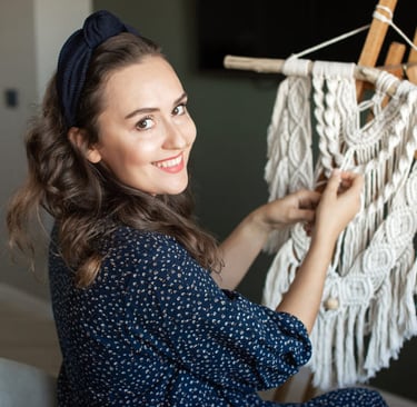 Mujer sonriente creando una pieza de arte decorativa estilo bohemio en macramé, utilizando cordón.