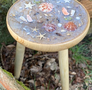 a small table with top inlay of shells atop the sand and set in resin