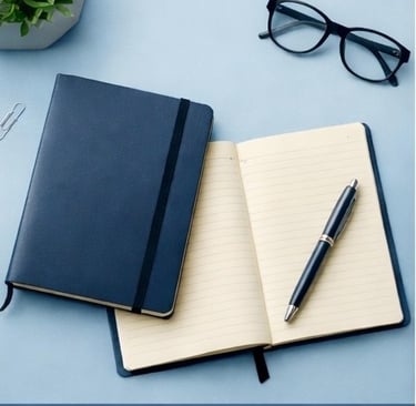 Cuadernos de diario de cuero azul con un bolígrafo y gafas en un escritorio de oficina minimalista.