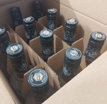 Een doos met premium House Pour vodkaflessen, voorzien van zwarte etiketten en doppen, klaar voor di