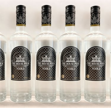 Een rij van acht heldere glazen flessen "The House Pour Vodka" op een witte achtergrond, waarop het 