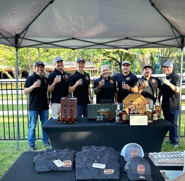 Bullets & Bourbon members standing together holding glasses of bourbon behind a table of different bourbon bottles
