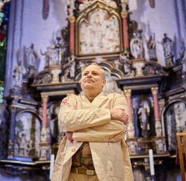 Ein Schauspieler vor einem Altar mit den Armen vor dem Körper.