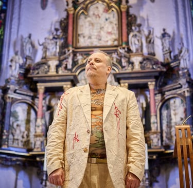 Ein Schauspieler vor einem Kirchenaltar. Er schaut in die Ferne.