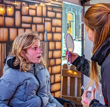 Een kind met roze gezichtsschmink kijkt met een verbaasde blik in een handspiegel die wordt vastgeho