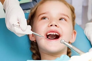 Una niña feliz recibiendo una revisión dental con un espejo bucal y herramientas de odontopediatría.