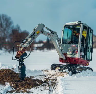 Excavator digging a post hole through frozen ground to reach the frost line for structural stability