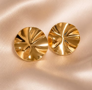 Pair of textured gold disc stud earrings resting on elegant champagne silk fabric.