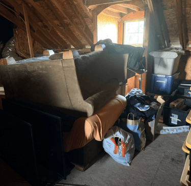 An attic with a bunch of junk: couch, chair, garbage bags