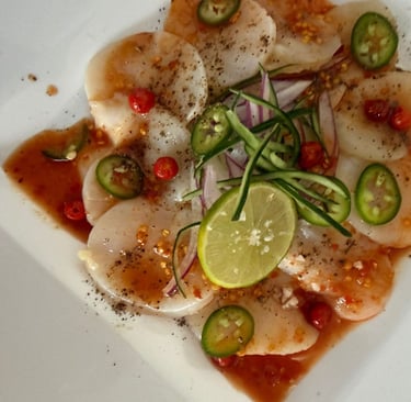 Aperitivo de carpaccio de vieira fresca con lima, rodajas de jalapeño y salsa de chile, servido.