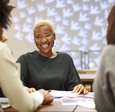 Una mujer afro con una camisa verde sonríe y habla con otras mujeres