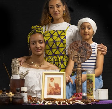 Three women posing behind a spiritual altar with an African wood carving and sage.