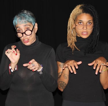 Dos mujeres actrices migrantes con camisas negras y gafas actuan como posando para la foto